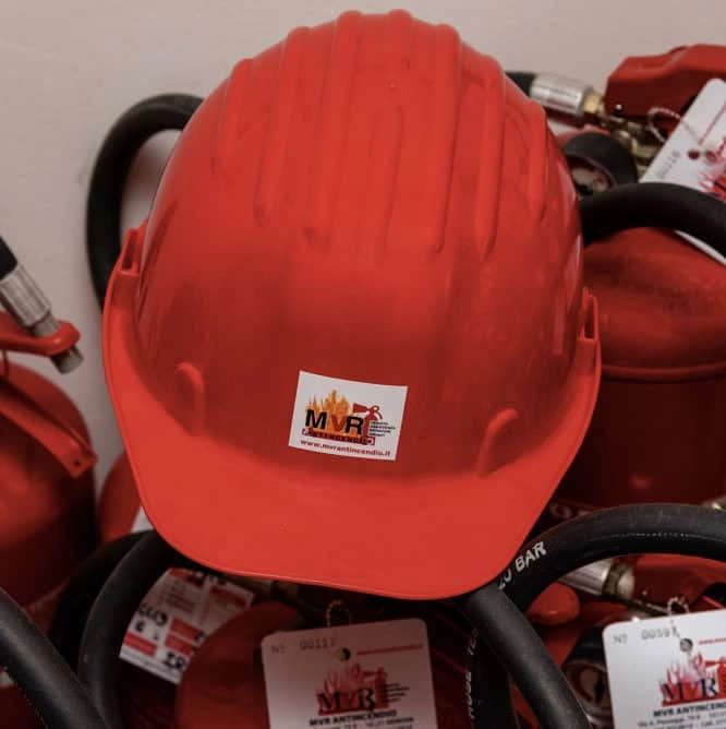 Elmetto di protezione con marchio MVR Antincendio appoggiato su una fila di estintori